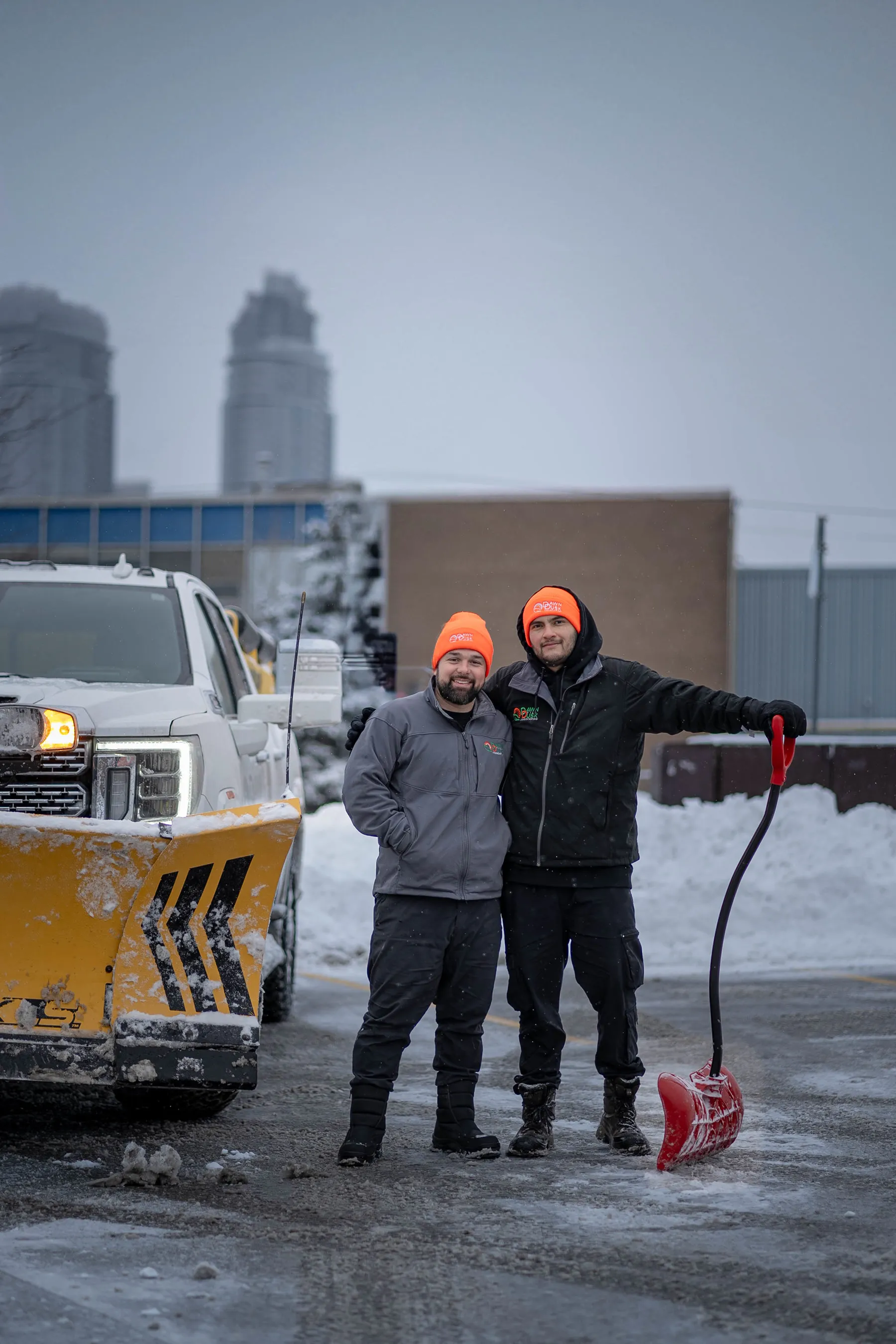 Dawn Till Dusk crew standing with the plow truck on a snowy commercial lot