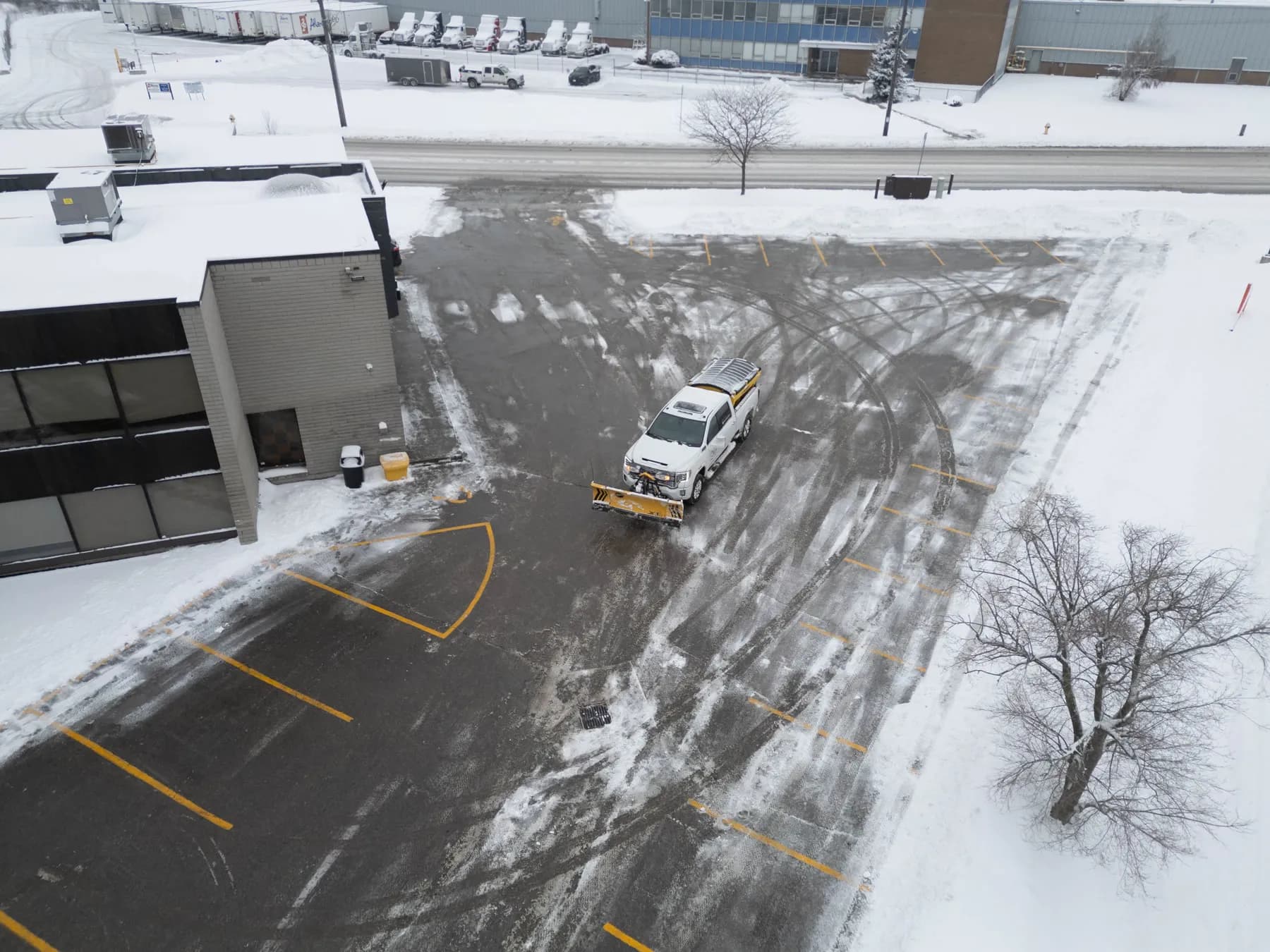 Drone view of a Dawn Till Dusk plow truck clearing a snow-covered commercial parking lot in Scarborough