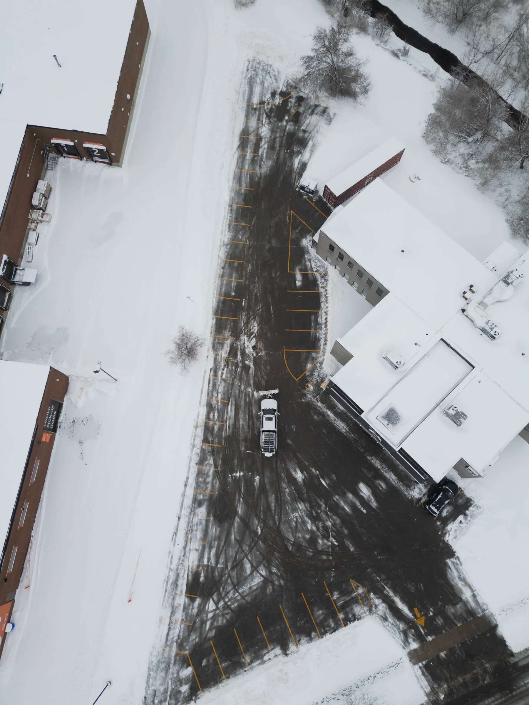 Overhead drone shot of commercial lot snow plowing in progress